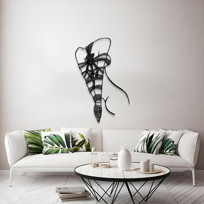 A modern living room scene featuring a black metal wire wall art piece shaped like a stylized ribbon or bow, mounted on a light gray wall above a white sofa with green leaf-patterned pillows.