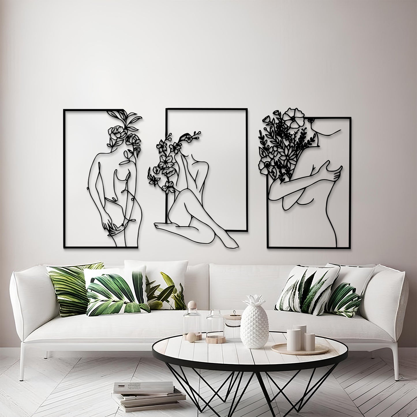 Three framed black metal wall art prints depicting minimalist line-art female figures with flowers, displayed above a white sofa in a modern living room setting.
