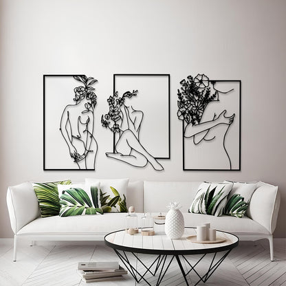 Three framed black metal wall art prints depicting minimalist line-art female figures with flowers, displayed above a white sofa in a modern living room setting.