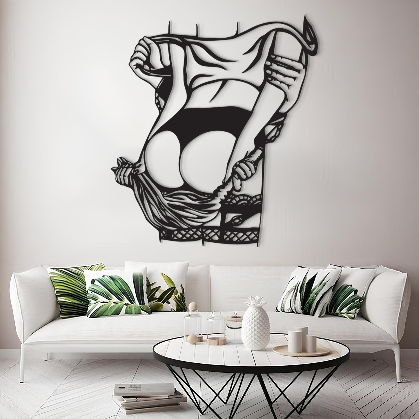 A black metal wall art piece depicting a stylized figure lifting a garment, displayed above a white sofa in a modern living room setting.