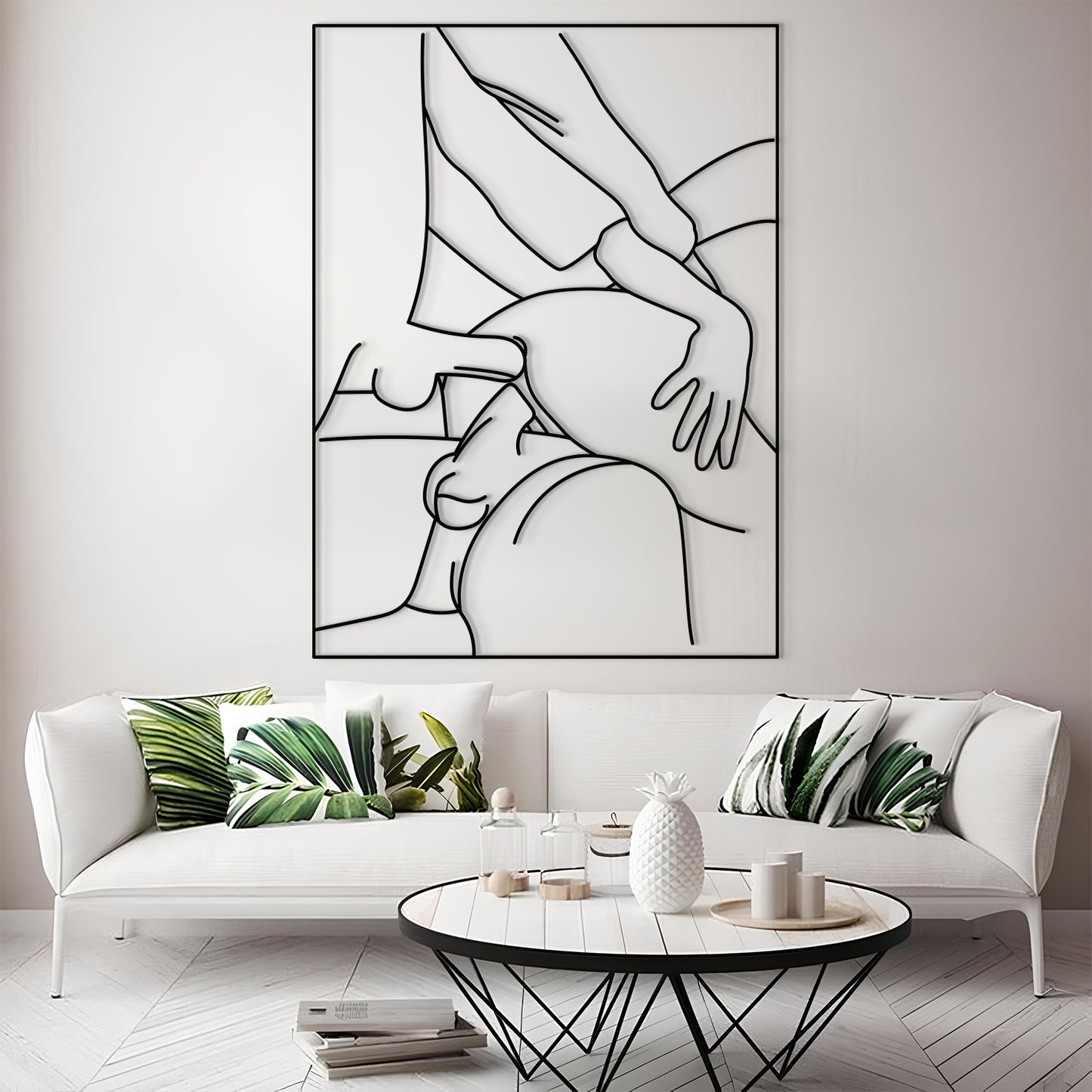 A modern living room scene featuring a large black and white minimalist line art print of a couple on the wall above a white sofa with green leaf-patterned pillows.