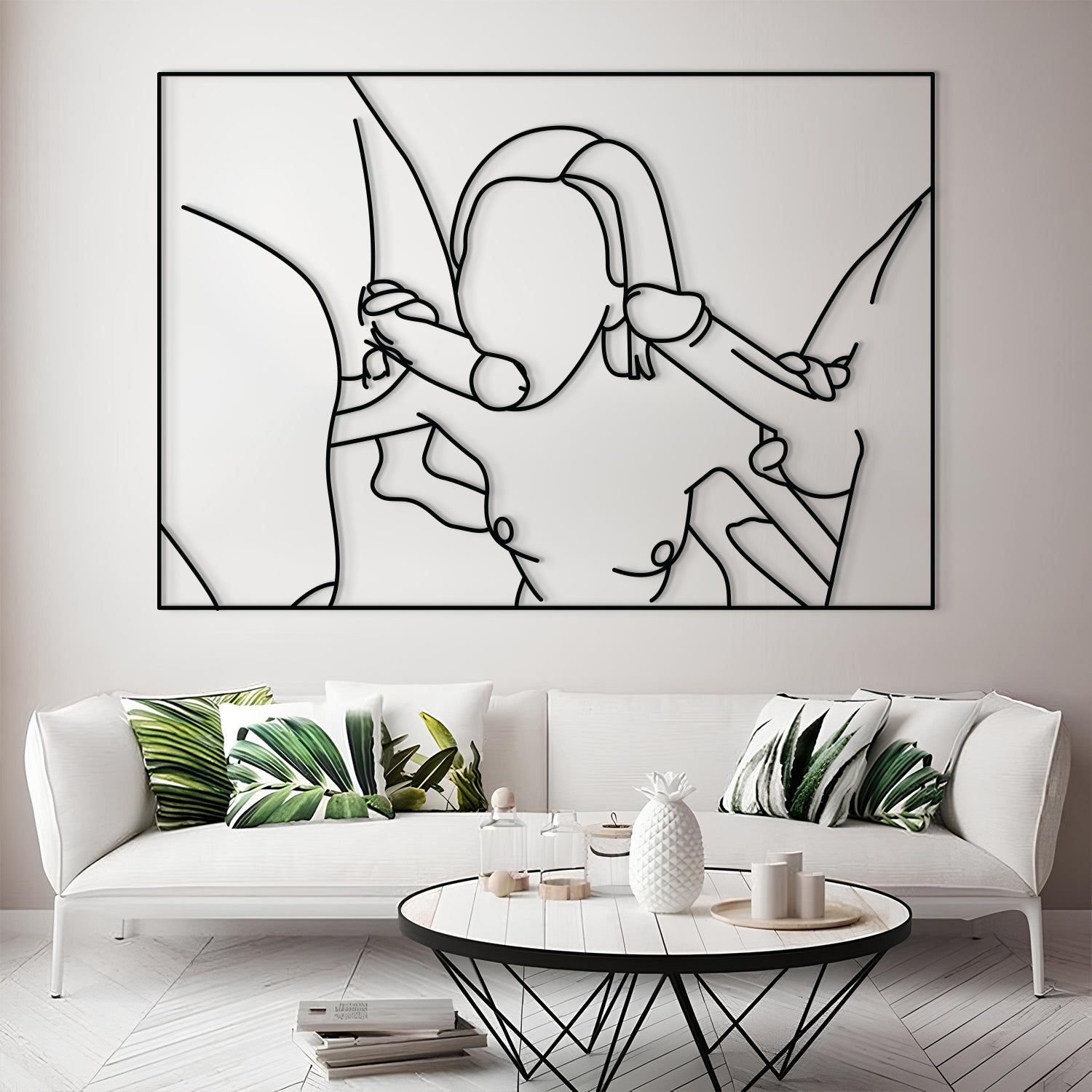 A large black and white minimalist line art wall sculpture depicting a couple embracing, mounted on a light gray wall above a modern white sofa with green leaf-patterned pillows.