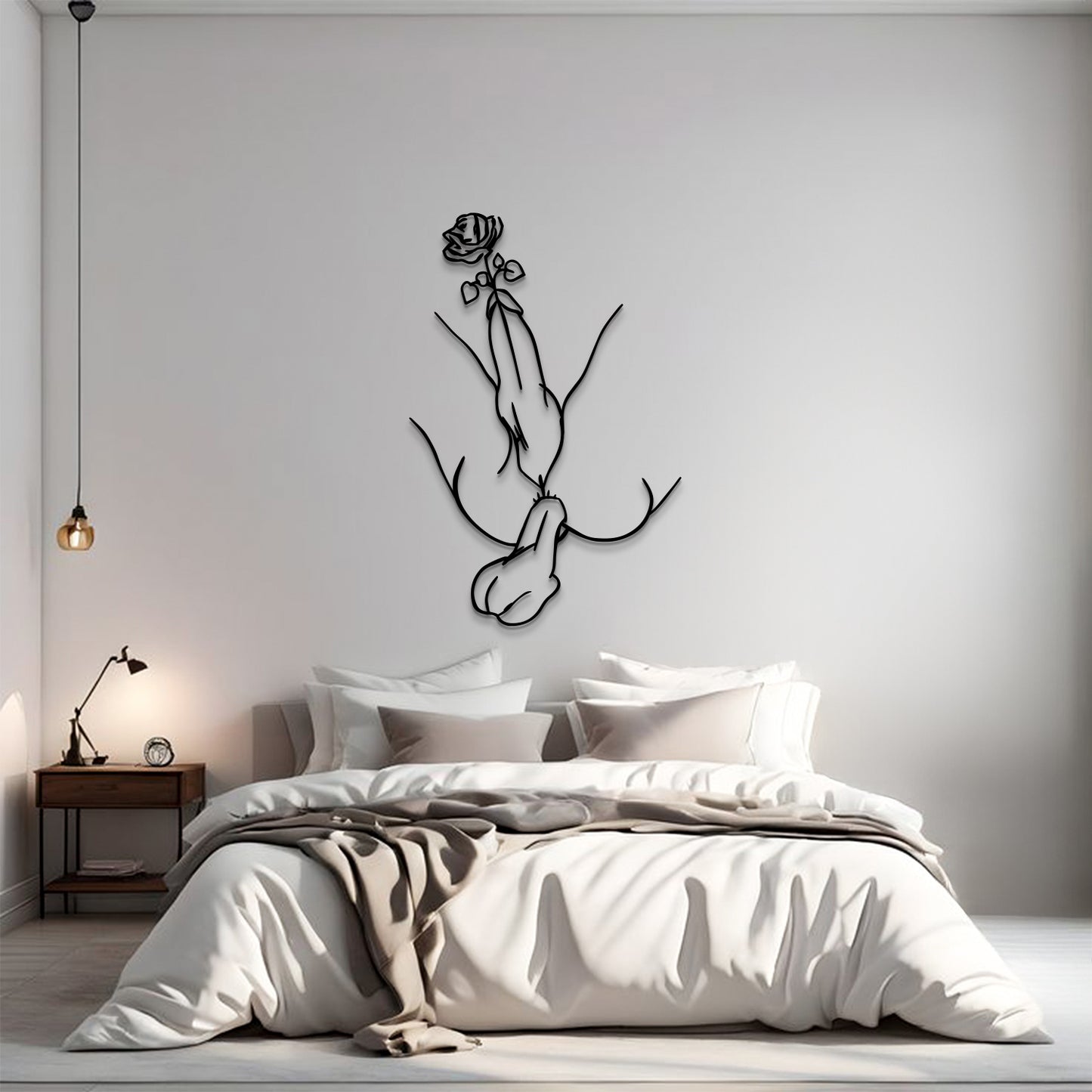 A minimalist bedroom scene with a bed dressed in white and beige linens, a small wooden nightstand with a lamp, and a black line-art wall sculpture of hands holding a rose mounted on the wall above the bed.