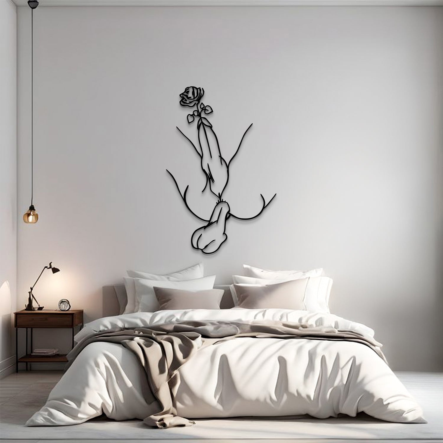 A minimalist bedroom scene with a bed dressed in white and beige linens, a small wooden nightstand with a lamp, and a black line-art wall sculpture of hands holding a rose mounted on the wall above the bed.