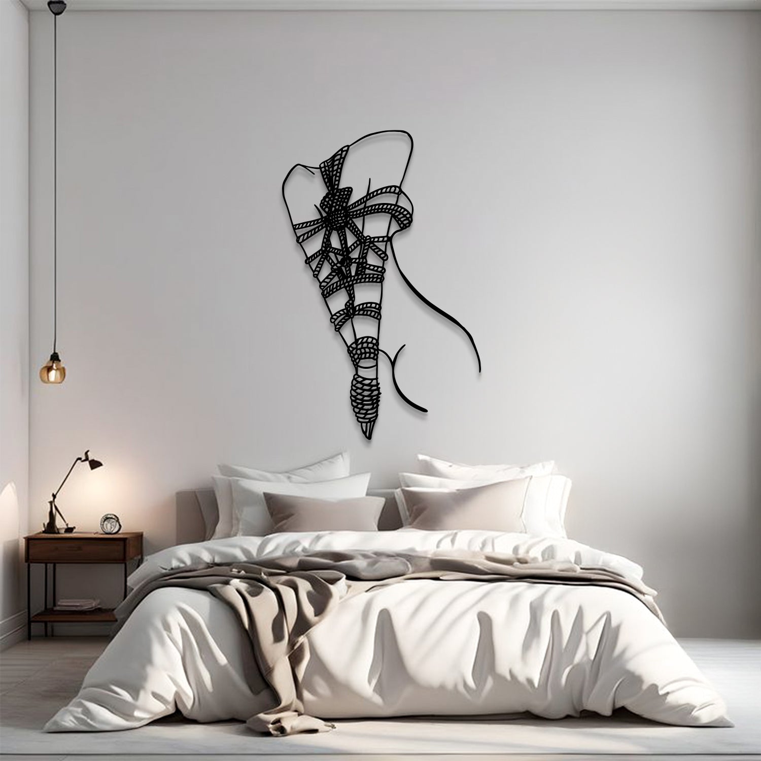 A modern bedroom scene with a bed dressed in white and beige bedding, a small wooden nightstand with a lamp, and a black wire wall art piece shaped like a stylized ribbon bow on the wall above the bed.