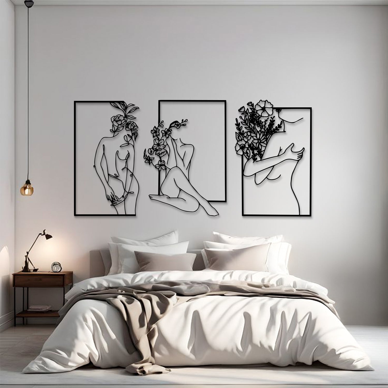 A modern bedroom scene with a bed dressed in white bedding and a beige throw, beneath three framed black line-art wall art prints showing abstract female figures and floral line drawings on a light gray wall.