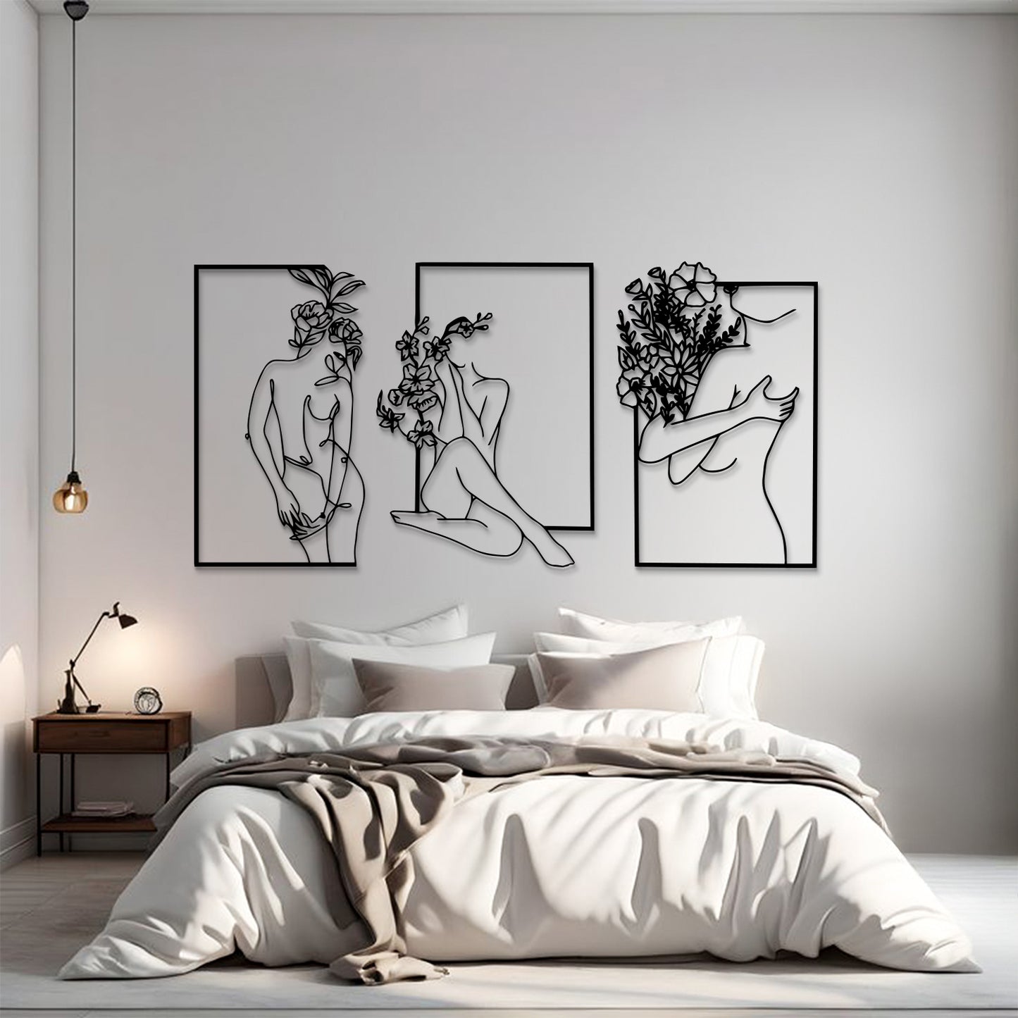 A modern bedroom scene with a bed dressed in white bedding and a beige throw, beneath three framed black line-art wall art prints showing abstract female figures and floral line drawings on a light gray wall.