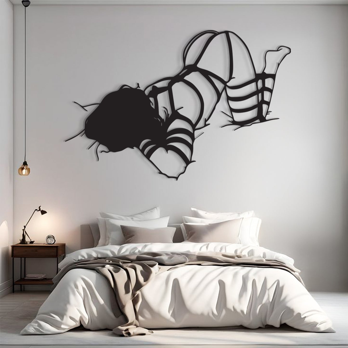 A modern bedroom scene with a bed dressed in white and beige bedding, a small wooden nightstand with a lamp, and a large black abstract wall sculpture above the bed on a light gray wall.
