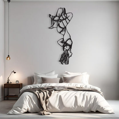 A modern bedroom scene with a bed dressed in white and beige bedding, a small wooden nightstand with a lamp, and a large black abstract wall sculpture mounted on a light gray wall above the bed.