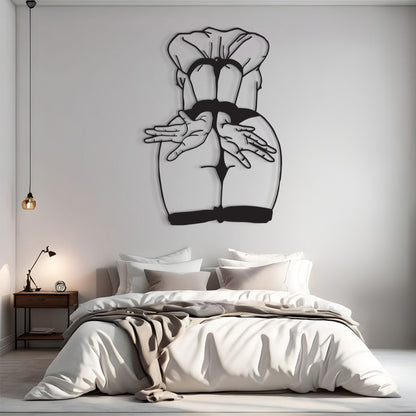 A modern bedroom interior with a large black metal wall art piece depicting a stylized female back and hands, mounted above a bed with white bedding and a wooden nightstand.